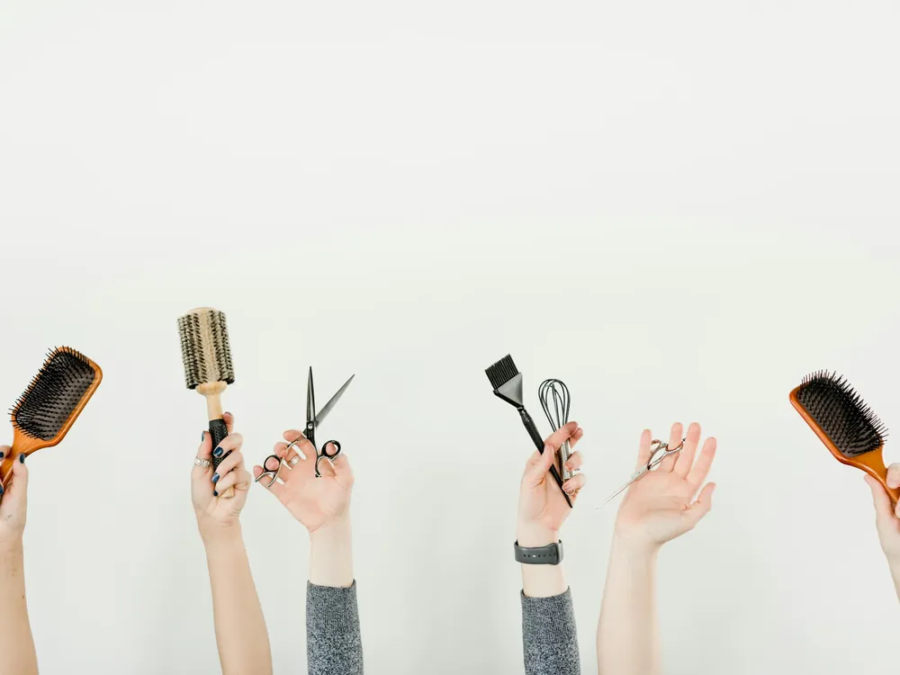 Hands holding brushes, scissors and a tint brush